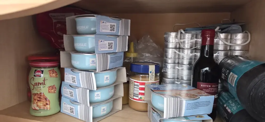 Vorratsfach mit gestapeltem Thunfischsalat, einer Großpackung Teelichter, Masken, Müllbeuteln und Erdnussbutter