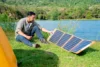 Mann beim Camping auf der Wiese mit einem Solarpanel